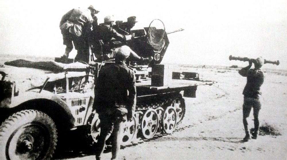 1941年,利比亚,一辆正在向敌军车辆开火的德军第606轻型防空营Sd.Kfz.10/4半履带防空炮车。注意有一位站在车旁的指挥人员在使用测距仪测量校对目标的着弹点。