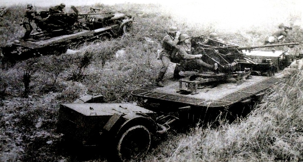1941年,东线苏联战场,德军两辆挂载了Sd.Anh 51拖车(装载弹药)的Sd.Kfz.10/4半履带防空炮车从伪装阵地驶出向敌军开火。