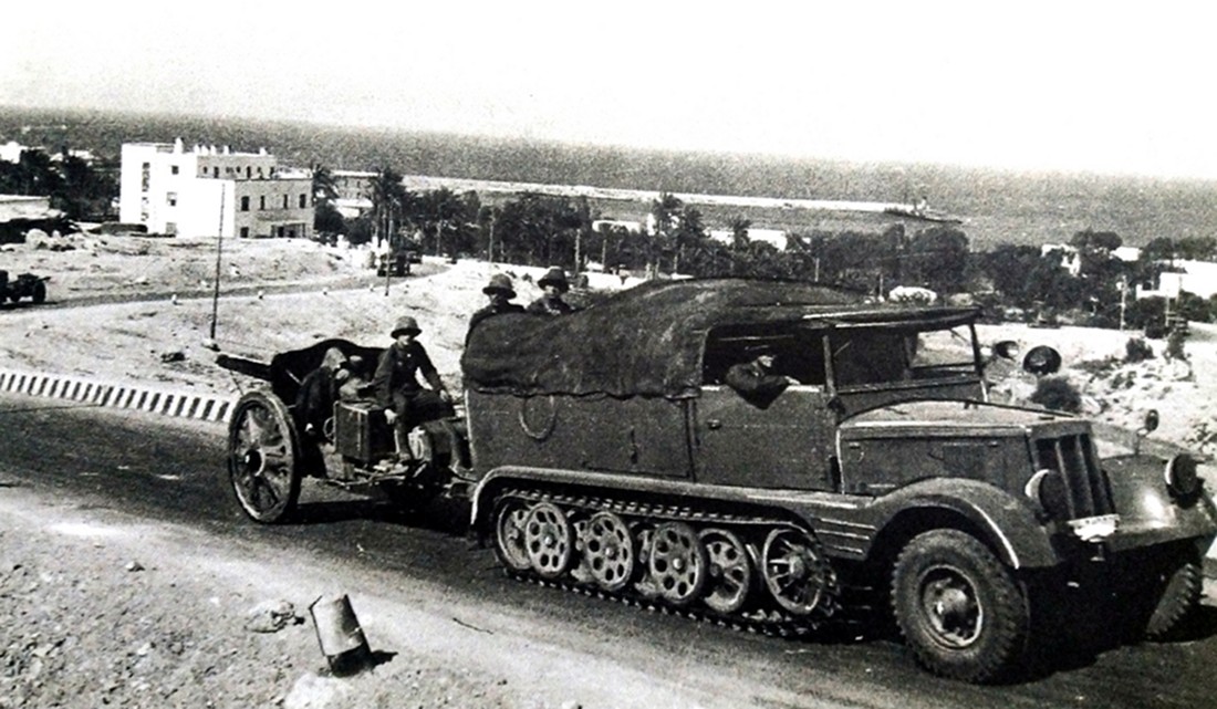 1941年,非洲战场,德军第5轻摩托化师75炮兵团1营的一辆3吨级Sd.Kfz.11(H Kl 6)半履带车拖带着一门105毫米leFH 18型榴弹炮在利比亚行进。
