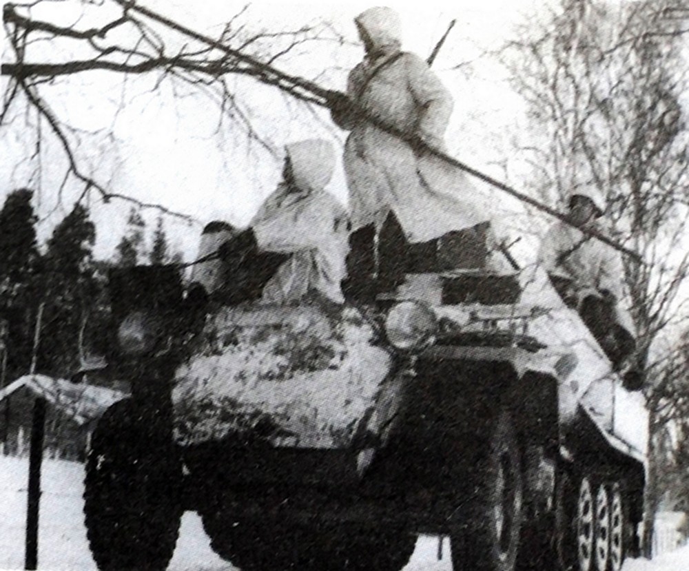 一辆德军Sd.Kfz.250/11半履带装甲野战电话布线车正在作布线操作，车上的一名布线兵正用一条长杆将车头滚轴的线缆往树上铺设。