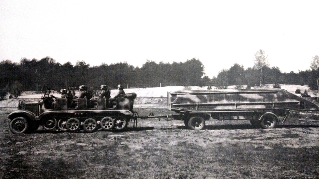 一辆5吨级的Sd.Kfz.6半履带牵引车正拖挂着一辆浮桥拖车行进,图中Sd.Kfz.6半履带牵引车的挡泥板类型较为少见。