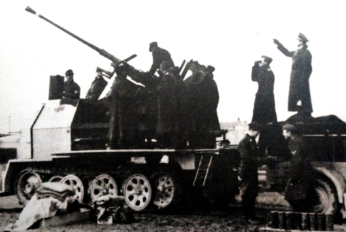 一辆德国空军的Sd.Kfz.7/2半履带防空炮车正在军官指挥下作战斗准备，该炮车后部挂有用于存放弹药Sd.Ah 57弹药车。