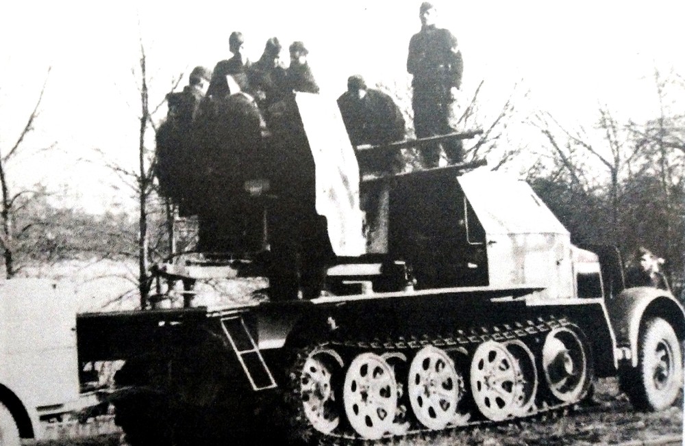 1943年底生产的Sd.Kfz.7/1半履带防空炮车，它的驾驶舱室和车前格栅已经加装了80毫米厚的装甲钢板。图中这辆炮车有7名车组成员，炮车正停靠在一树林边空地上，以保证火炮有良好的视野。