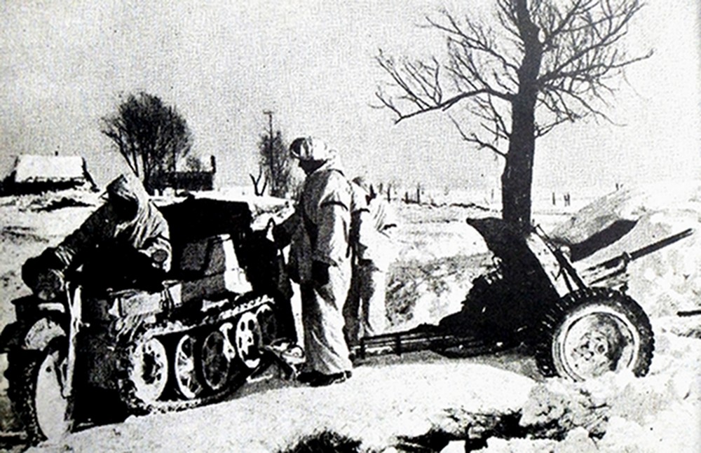 1941年冬季,东线苏联战场,一辆德军Sd.Kfz.2小型半履带车在雪地上准备将一门37毫米反坦克炮拖离阵地,德军士兵臂上都绑着的红色识别带,这是为了与同样穿着白色冬季伪装服的敌方士兵作出识别。