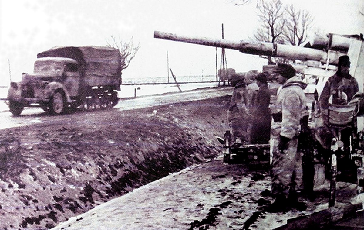 守卫在公路旁的一门德军88毫米Flak36/37高射炮,一辆福特V3000S(Sd.Kfz.3)军车在88毫米炮前方道路驶过。