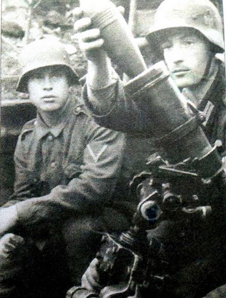 二战早期东线战场,战斗中,德军一个80毫米GrW34迫击炮班士兵正在将炮弹放入炮筒进行发射。这些士兵还穿着较早发行的绿色带领上衣。其中一名的衣袖上还佩有一个燕尾V字形的徽章布,证明这是一个服役期不少于6年的老兵。