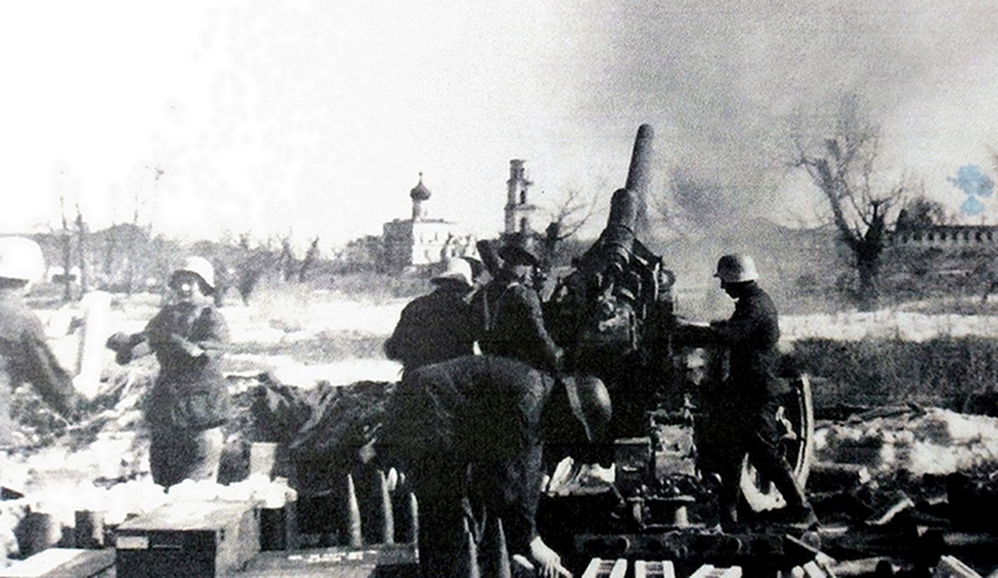 二战东线苏联战场，德军炮兵连阵地，正在投入激战的一门150毫米s.FH18榴弹炮，炮组成员有的负责射击，有的负责准备炮弹。地上放置了大量弹药，弹丸装在木框容器内，弹药匣装在盒子中。