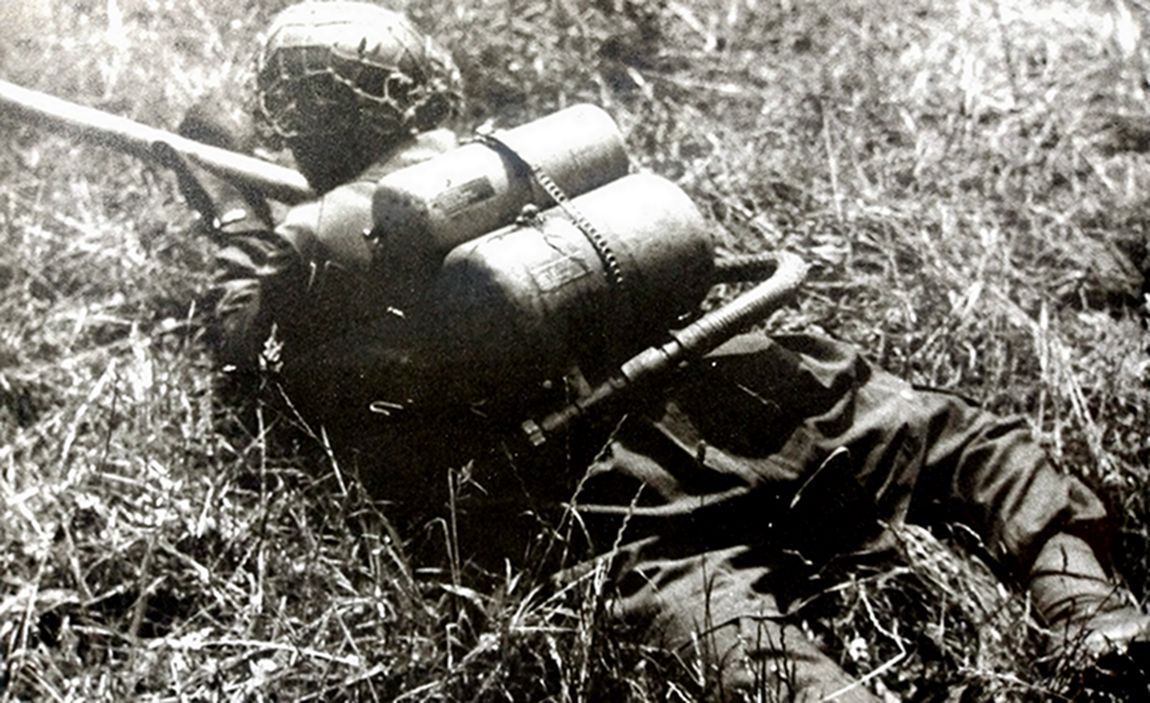 1944年,西线法国战场,一名装备41型火焰喷射器的德军士兵正埋伏在草丛中,准备对敌方发动攻击。