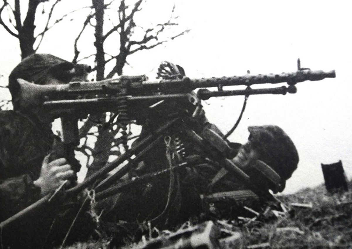 1940年5月，西线法国战场，一个德国武装党卫军的MG34重机枪组正在阵地上作战，MG34机枪支在三脚架上，一弹药手伏在机枪旁用子弹链给机枪供弹。