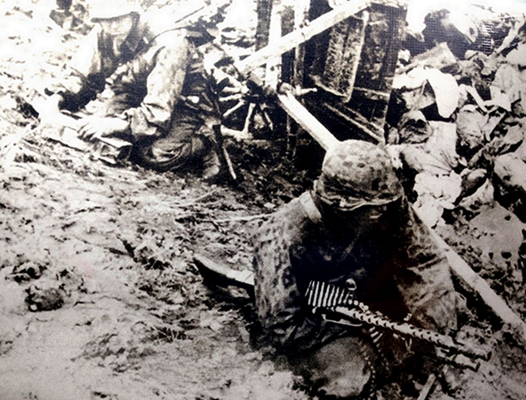 1941年10月，东线苏联战场，在德军的「台风」战役中，德国中央集团军群正发动全力向苏联首都莫斯科进攻，德军的一个MG34机枪组正在废墟中转移前进阵地，前面的机枪射手抱着带子弹链的一挺MG34机枪，后面的弹药手则背着三脚架，手中拿着2个弹药箱。图中情景反映了当时战斗的激烈程度。