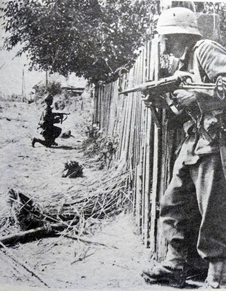 1944年7月,西线法国战场,在诺曼底登陆后的英军继续向卡昂挺进,但德国武装党卫军装甲师利用遍布灌木树篱的地形,进行了顽强的阻击。图中是手持MP40冲锋枪,利用灌木树篱地形的掩护与英军作战的德国党卫军士兵。