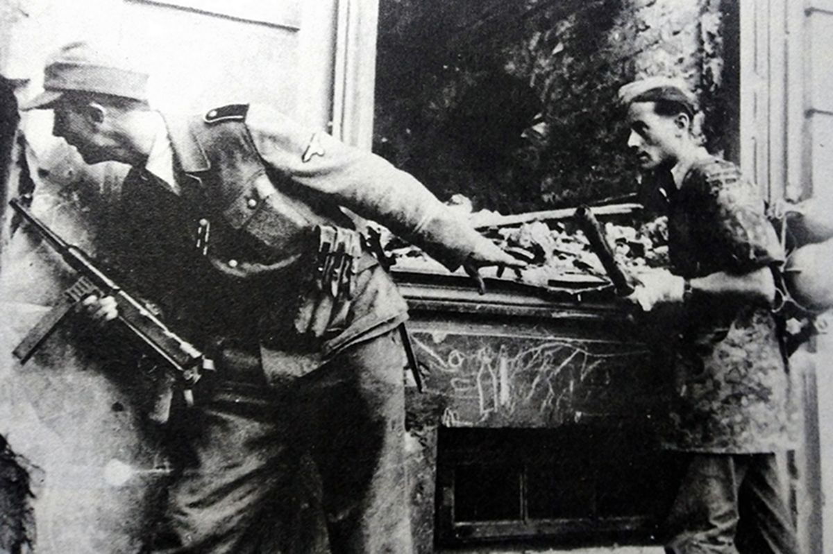 1945年4月,东线德国战场,一名手持MP40冲锋枪的德军士兵隐藏在房屋角落中紧张地进行观察,后面士兵手持着一支46型火焰喷射器,神情也十分紧张。