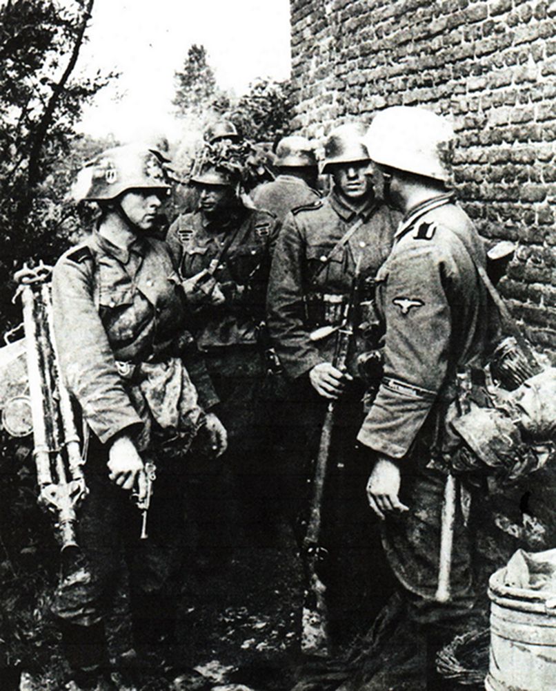 1940年,西线法国战场,一群隶属德国武装党卫军第5「维京」装甲师的官兵在战斗间隙中小憩,图中左边的一名士兵背着三脚架(用于安装MG34机枪作防空用),手中拿着一支自卫用的鲁格P08手枪。(注:实际上图中这支党卫军部队在几周后才正式命名为「维京」师)