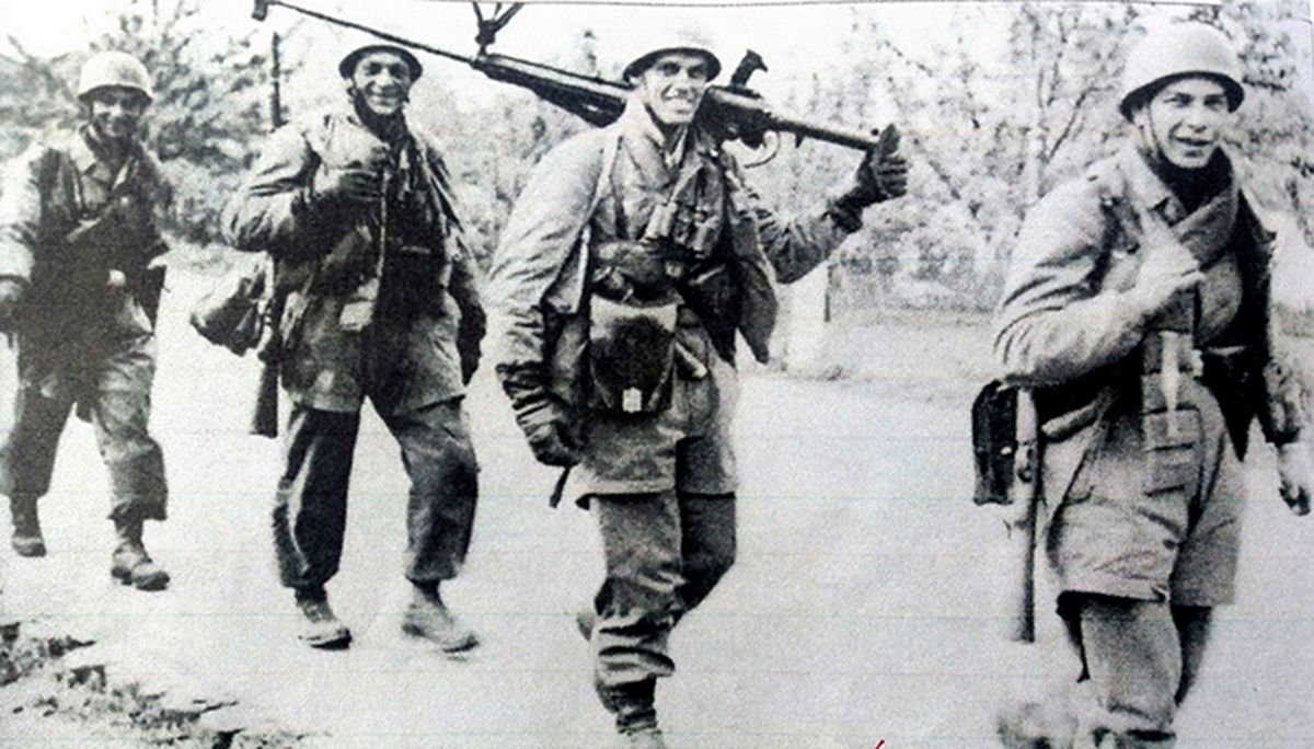 1940年,西线战场荷兰地区,一群全副武装的德军伞兵沿着荷兰的乡村小路前进,队伍中一人扛着PzB39型反坦克枪,由于战事顺利,士兵们都是开心轻松的表情。
