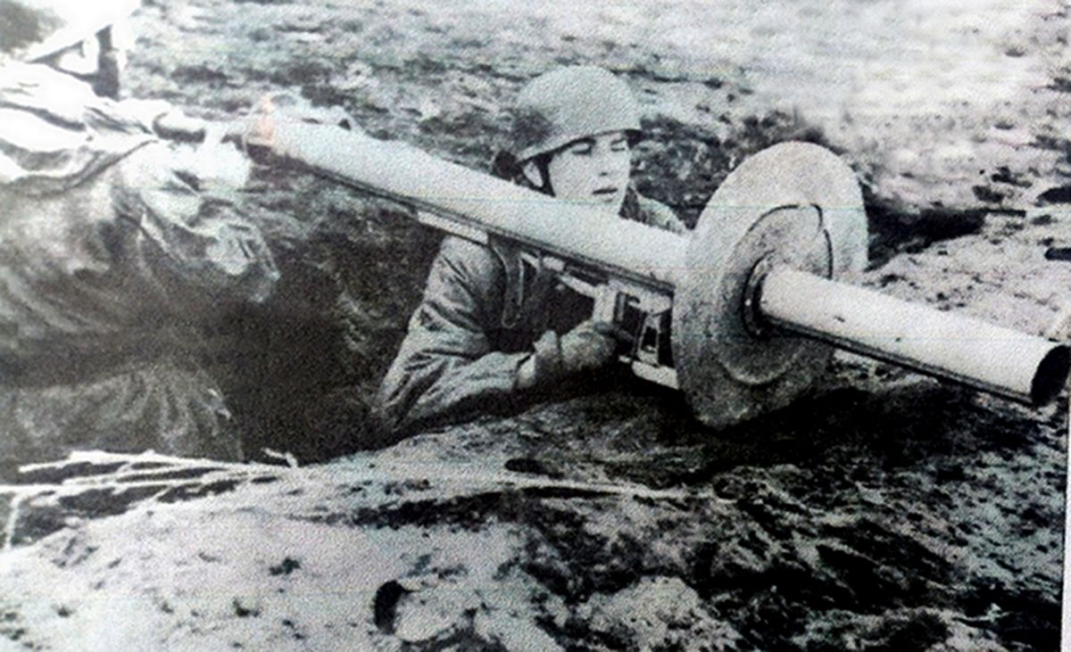 战壕中,两名德军伞兵准备用RPzB 54型「坦克杀手」反坦克火箭筒发射火箭弹射击敌方坦克,其中一名士兵负责装弹,另一名士兵手握板机正在瞄准。