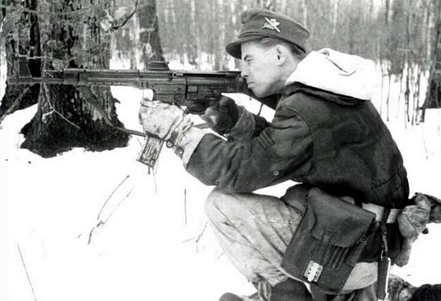 1944-1945年冬季,一名头戴野战帽的德国武装党卫军正手持StG44突击步枪跪在雪地上瞄准射击。