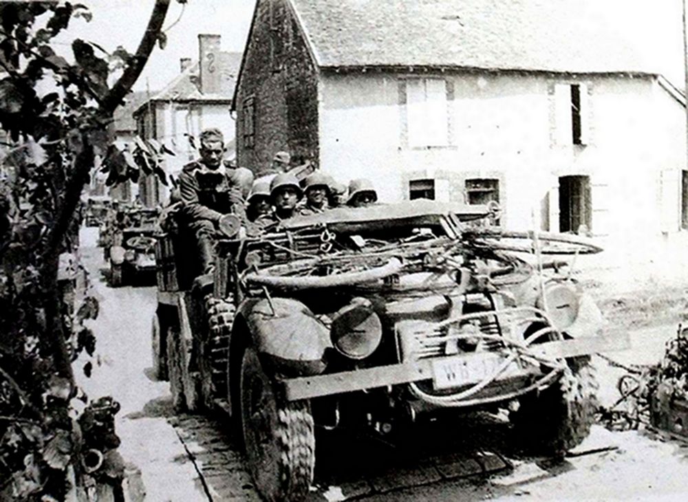 1940年，西线战场，一辆德军克虏伯 L2 H143轻型军用卡车满载着德军士兵行经法国一城镇。二战初期，该车大多作运兵车用。