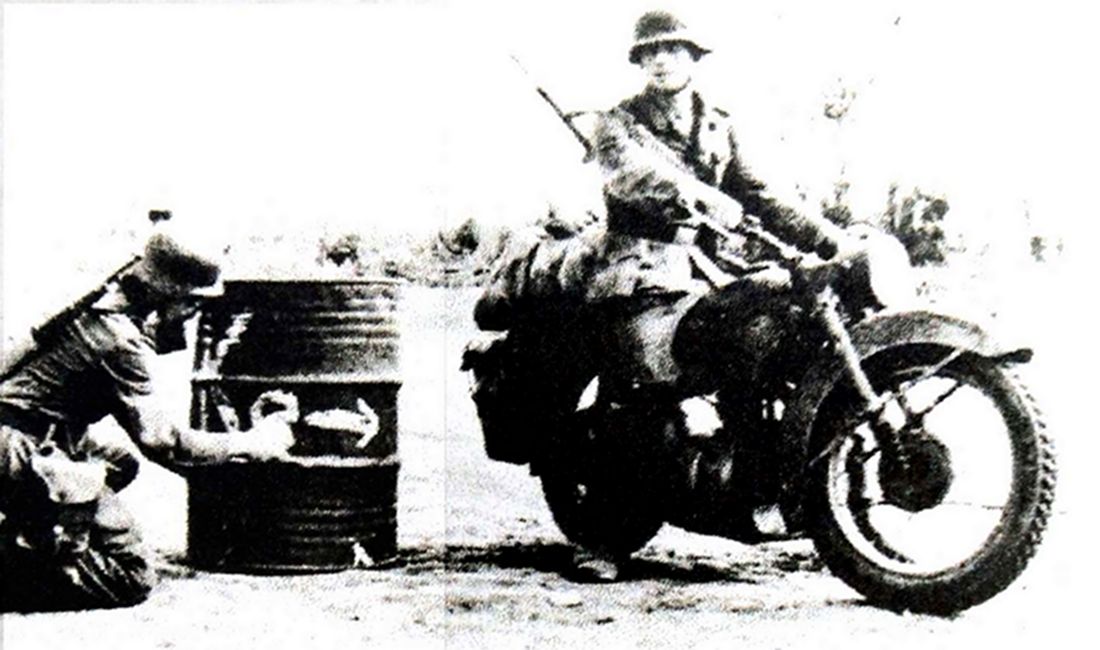 1941年夏天，东线苏联战场，驾驶宝马 R35轻型摩托车的德军传令兵正在路上观看写在油桶上的临时路标。