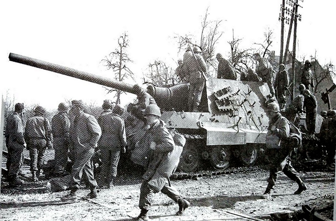 1945年3月德国本土战场，653重装甲歼击营遗弃在一铁路道口的编号234号「猎虎」重型坦克歼击车，该车已遭盟军摧毁，一群美军士兵正在查看这部「猎虎」残骸。