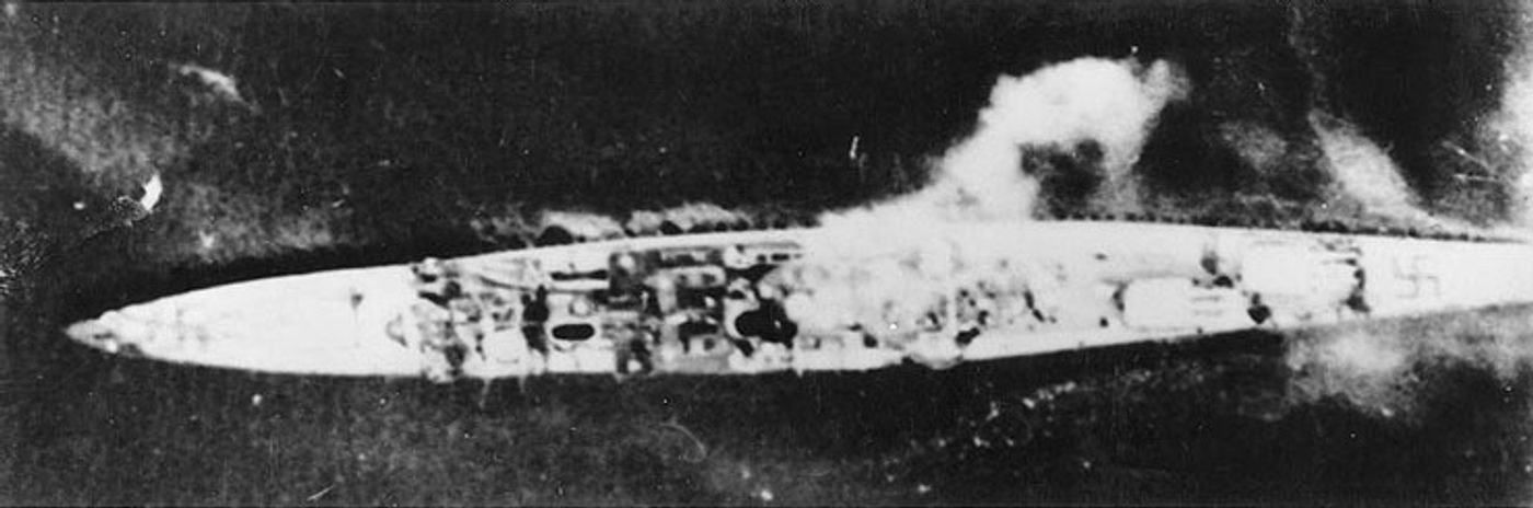 1940年4月10日，英国舰队航空兵攻击中的柯尼斯堡号。这张垂直俯拍照片摄于卑尔根港，可见舰首舰尾甲板上的纳粹卐字识别标志。当日清晨16架「贼鸥」式俯冲轰炸机自奥克尼群岛的哈特斯顿机场长途奔袭，命中数弹后这艘德国轻巡洋舰倾覆沉没，成为史上第一艘被空袭击沉的大型战舰。