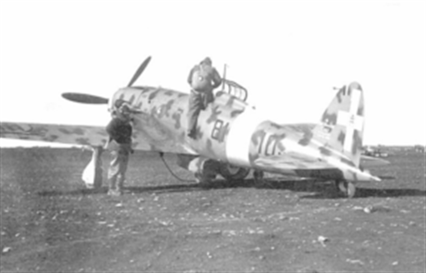 意大利皇家空军一架马基C.202「闪电」(机号84-10)停放在野战机场,地勤人员正协助飞行员登机,倒海鸥式机翼轮廓清晰可见。该机服役于北非或地中海战区的作战部队。