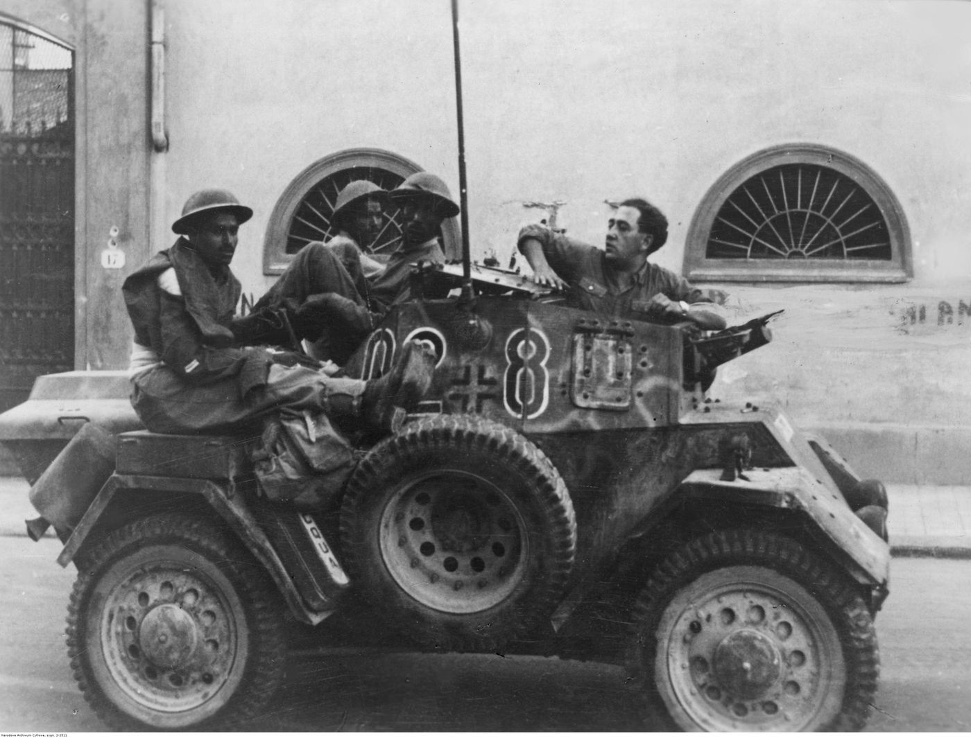 在博洛尼亚的街道上，一辆隶属于德军第13装甲师的 Panzerspähwagen Lince 202(i) 停在路边，三名被俘的廓尔喀士兵坐在发动机舱上。