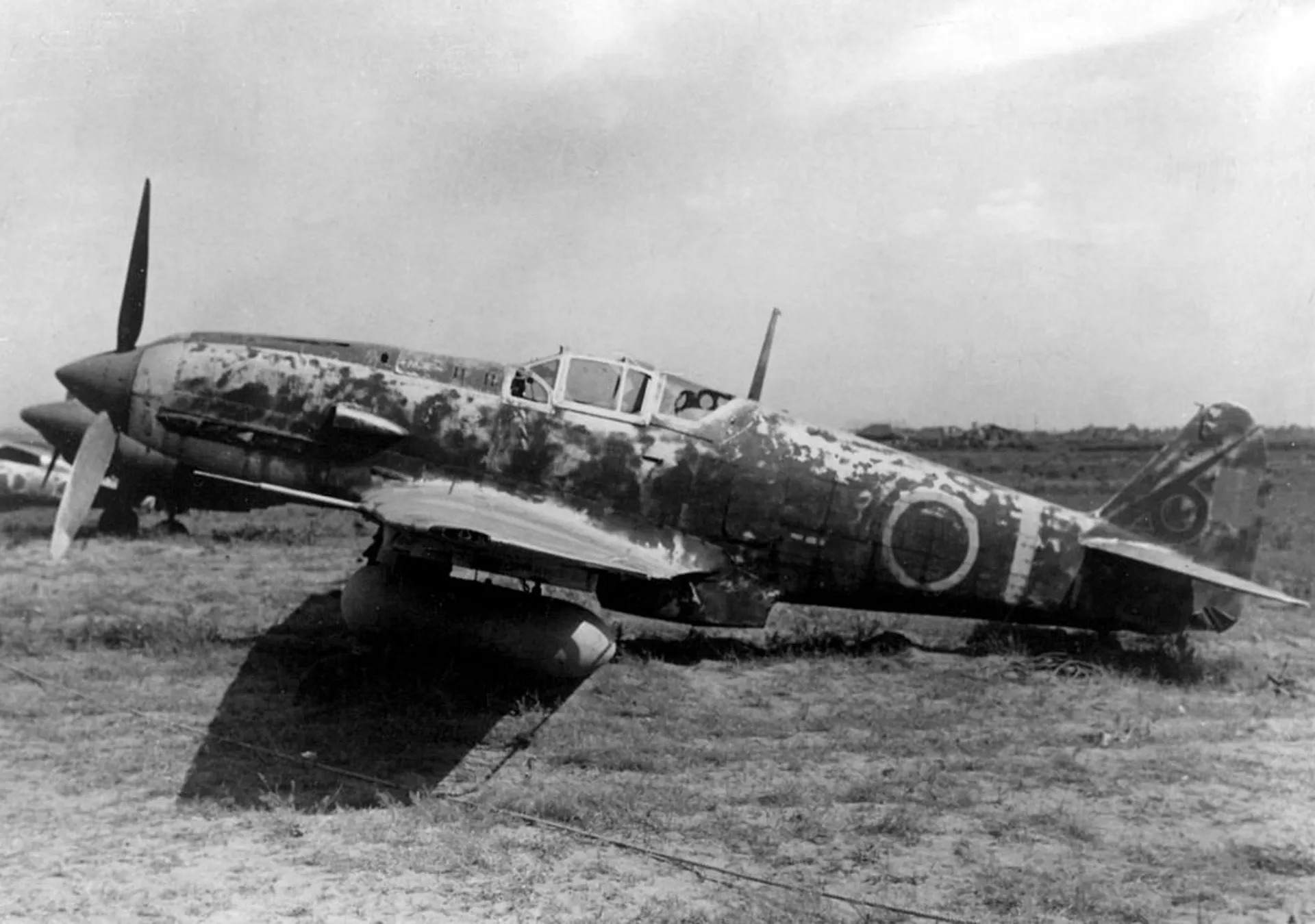 一架被遗弃的三式战斗机（Ki-61-I型），机身漆面大面积剥落、场地荒芜，反映了日军在太平洋战场上因燃料与零件短缺而被迫放弃战机的情景。