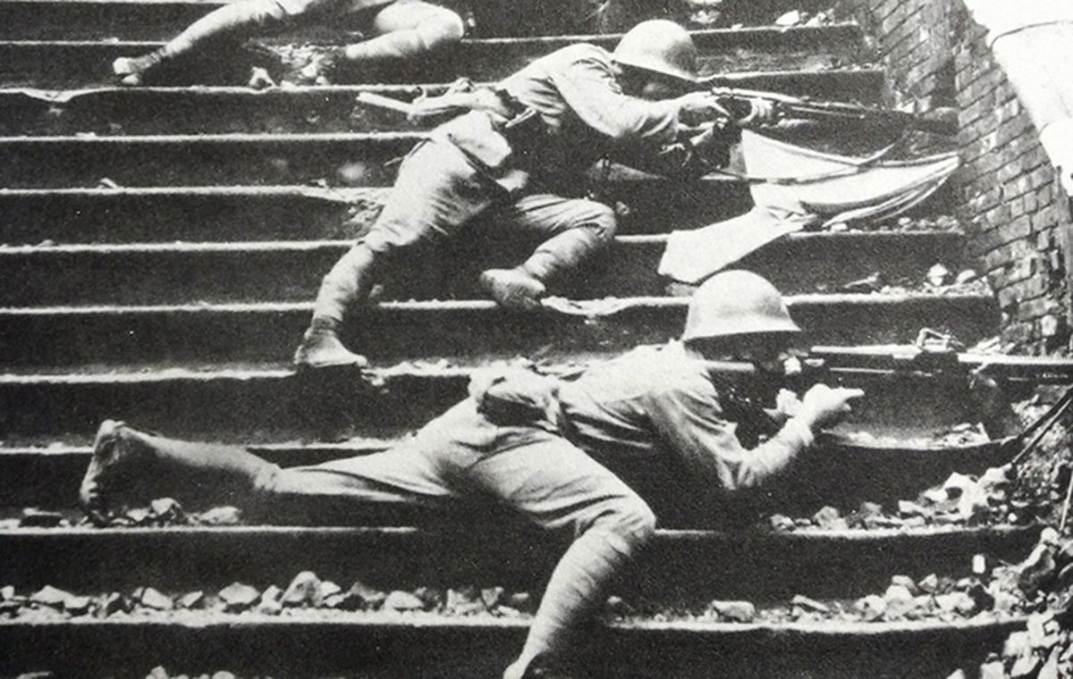1937年,中国抗日战场,淞沪会战期间,日军一名机枪手持11式轻机枪利用墙洞向中国军队射击。