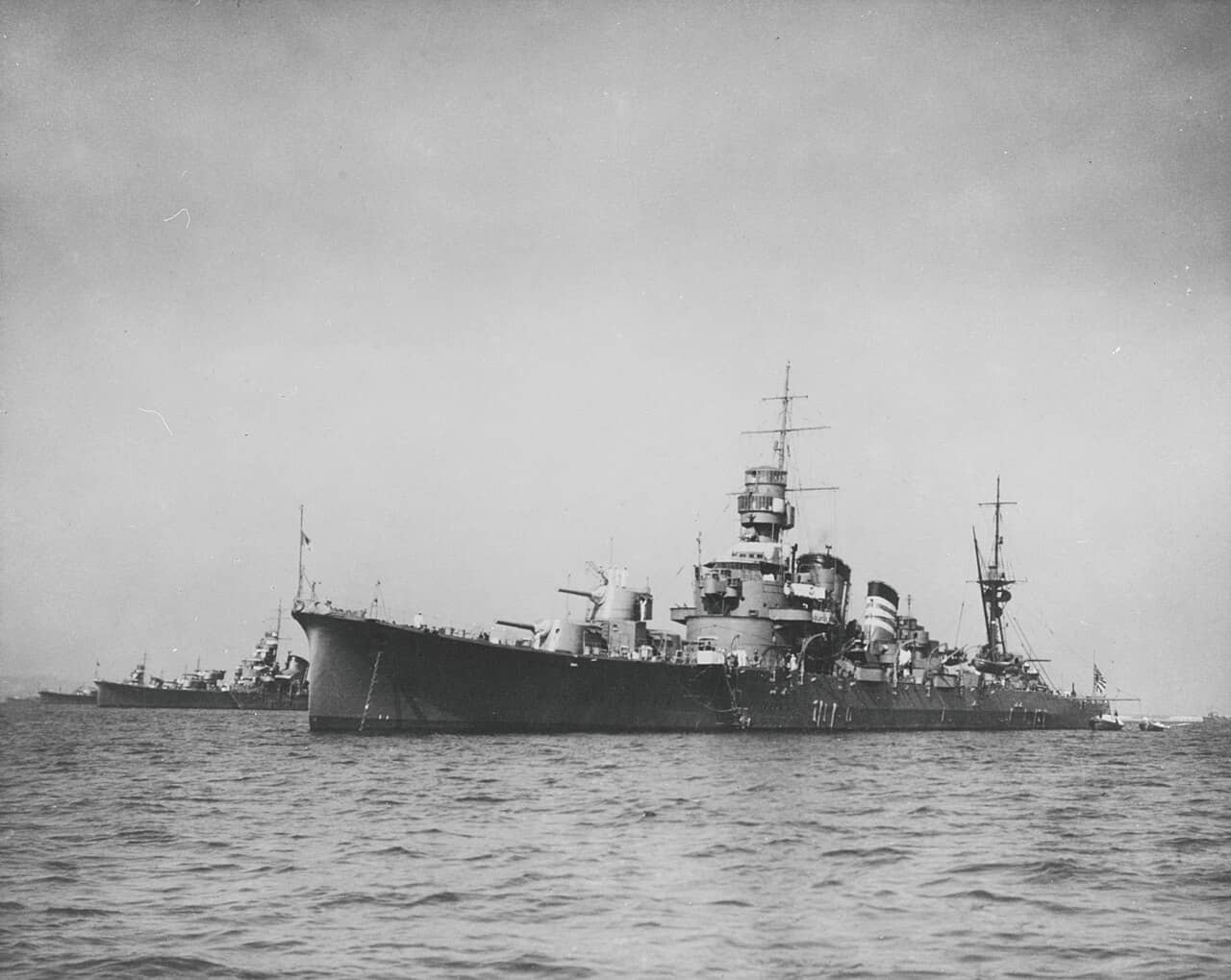 1935年10月4日至10日，古鹰号重巡洋舰锚泊于东京品川外海。烟囱上的三道白色环带表明她是第六战队的第三号舰；画面左侧远处可见同属第六战队的青叶号与衣笠号。