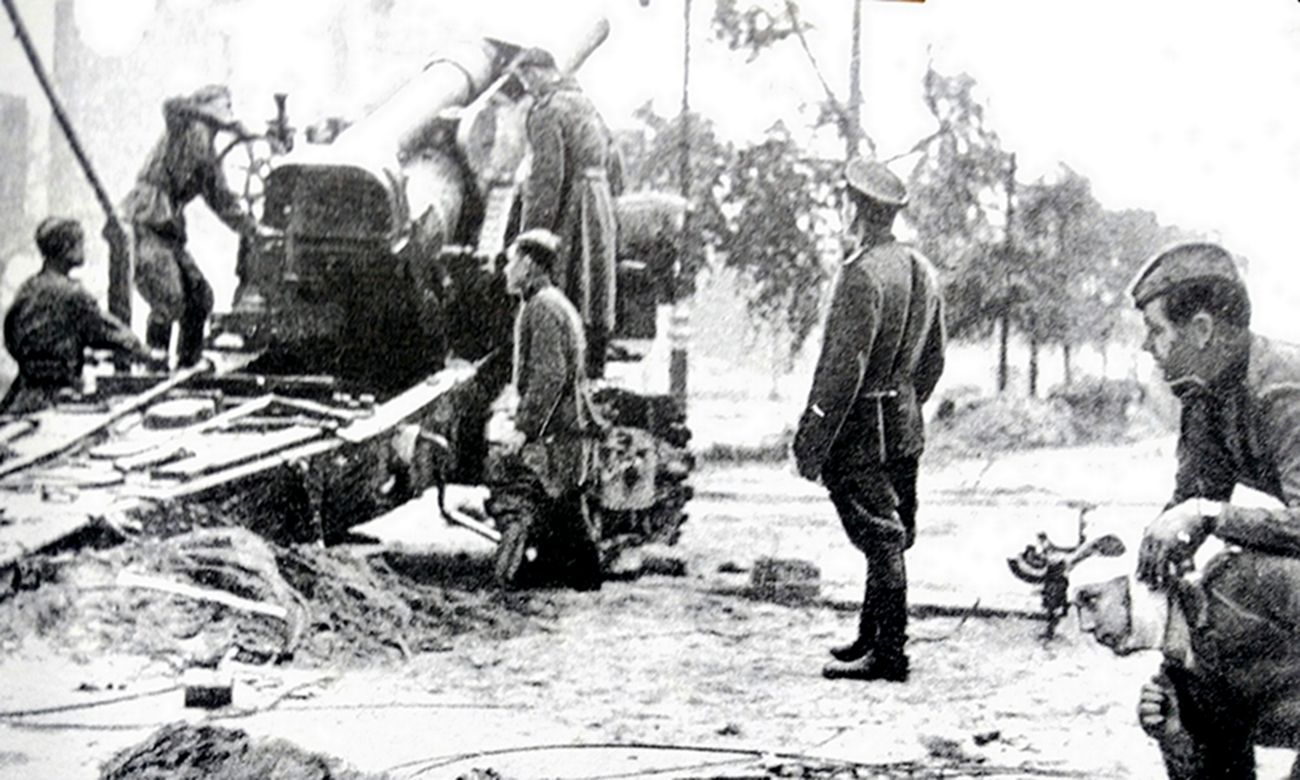 1944年,「苏德战争」期间,东线苏联战场,苏军一门1931式203毫米榴弹炮的炮兵正在炮长的指挥下将炮膛抬高,火炮右边的瞄准手正在大声报出调整角度,侧方一名站立的军官认真观察着火炮的炮管是否调整至射击角度。