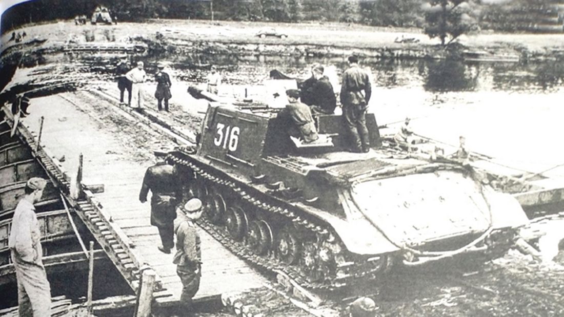 1944年4月，「苏德战争」期间，东线战场，苏军一辆ISU-122型自行炮车正通过一座由渡船临时搭建的桥向河对岸驶去。