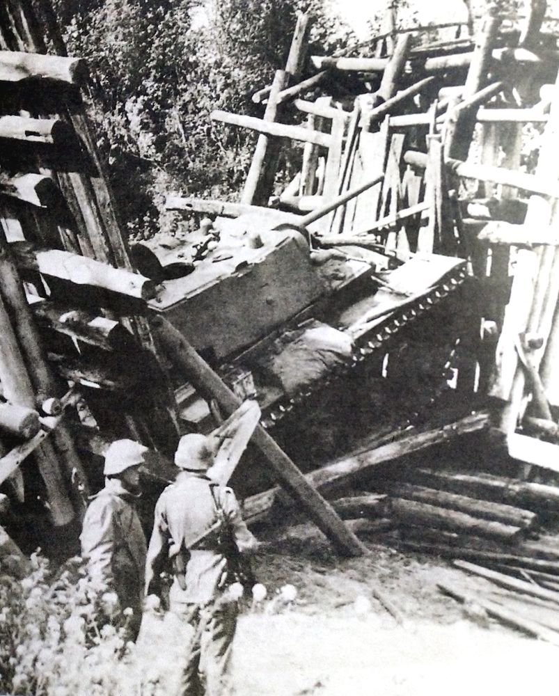 1942年夏季,「苏德战争」期间,苏联西部前线,两个德军士兵在观察一辆被压毁在木桥下的KV-1坦克(KV-1坦克车体过重,苏联很多道路与桥梁都因无法承受它的重量而塌毁,在无法拖救下只得将之放弃)。