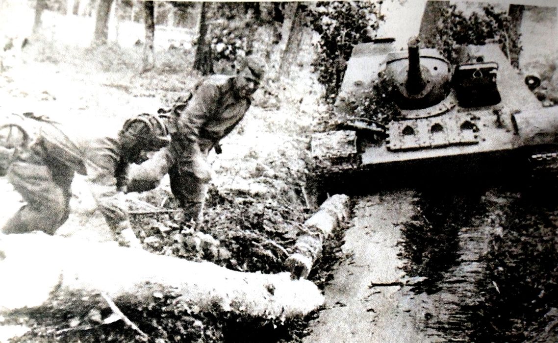 1944年6月，「苏德战争」期间，明斯克地区，白俄罗斯第1方面军的一辆苏军SU-85反坦克炮车陷入路沟中，车组乘员正在将树木填进路沟，以帮助炮车驶出。