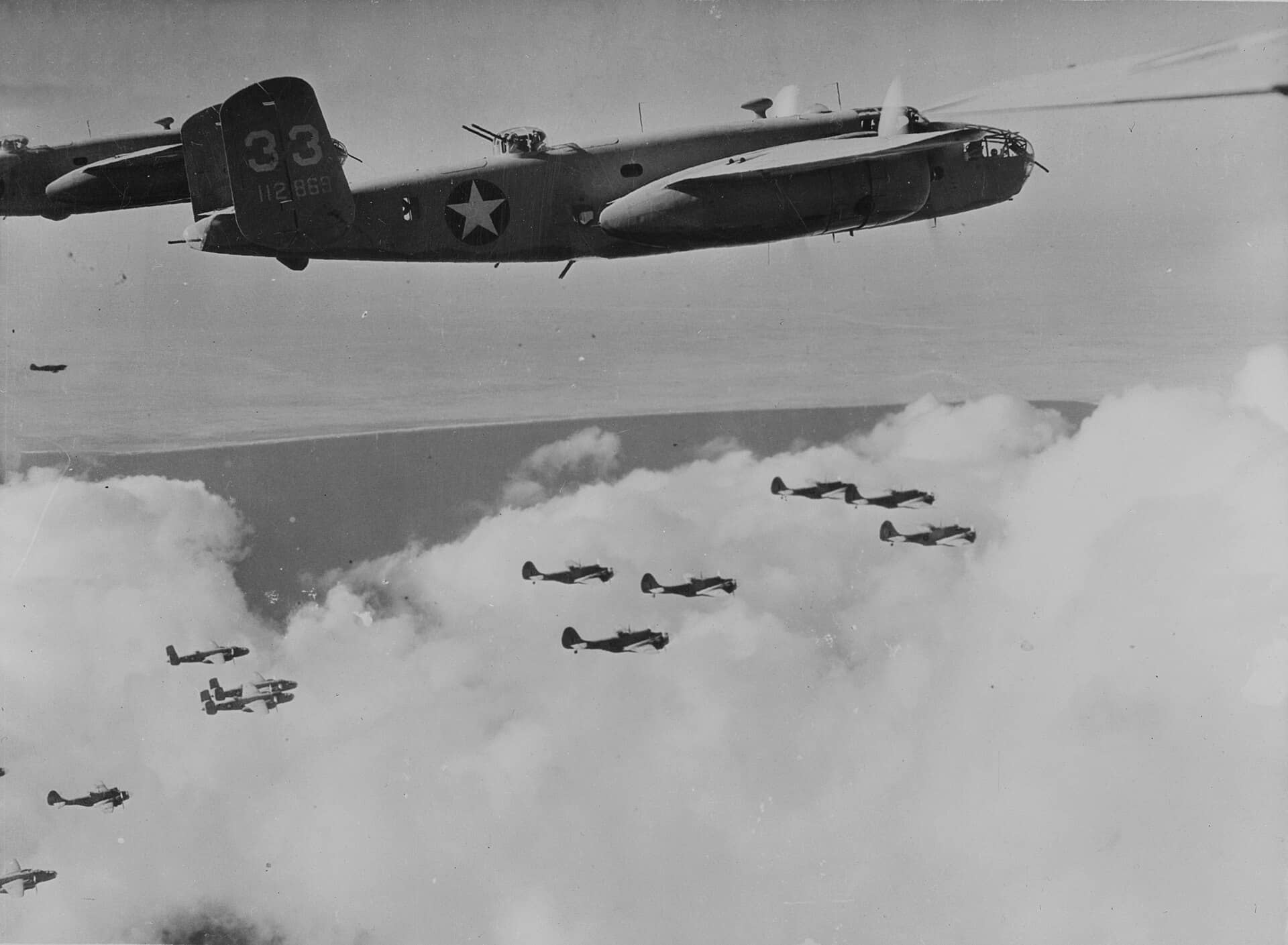 1943年,美国陆军航空队的B-25「米切尔」轰炸机群在北非上空编队飞行,画面下方可见伴随的护航战斗机。