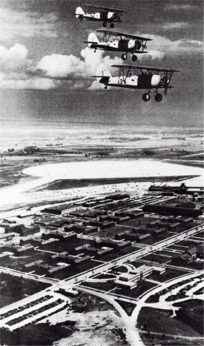 1940年代初,伊利诺伊州格伦维尤海军航空站(NAS Glenview)上空,三架 N3N 教练机编队飞越基地营区与机库。该站是美国海军预备航空训练的重要基地。