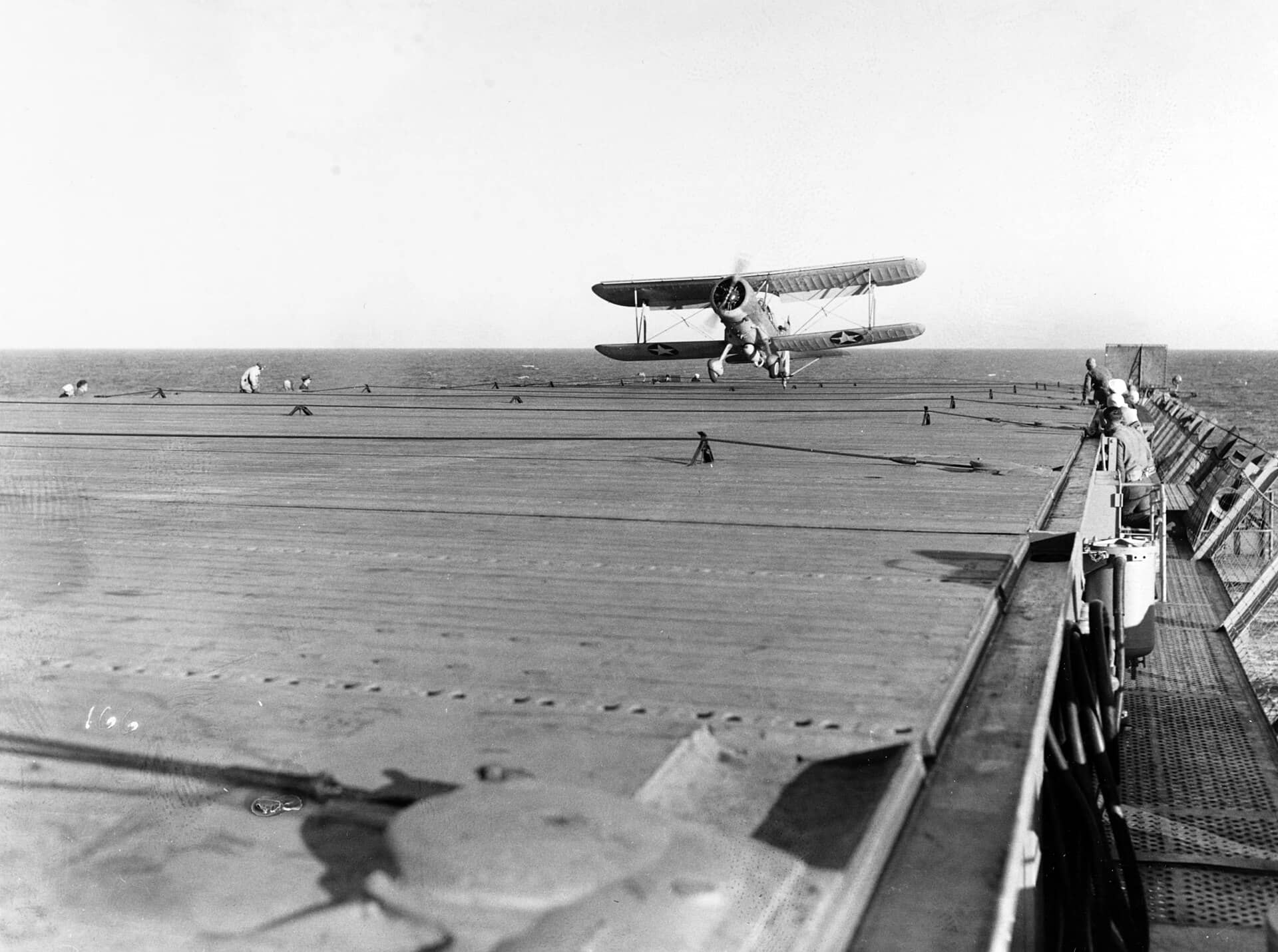 1942年6月17日,美国海军护航航母长岛号(AVG-1)上,一架第1辅助侦察中队(VGS-1)的SOC-3A「海鸥」正降落着舰,机腹挂架携带一枚深水炸弹。长岛号是第一艘投入反潜护航的美国护航航母。
