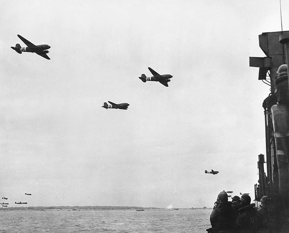 1944年6月6日前后,诺曼底登陆期间,美国陆军航空队的道格拉斯C-47「空中列车」运输机在犹他海滩外海低空飞越一艘由美国海岸警卫队负责操作的LCI(L)步兵登陆艇。