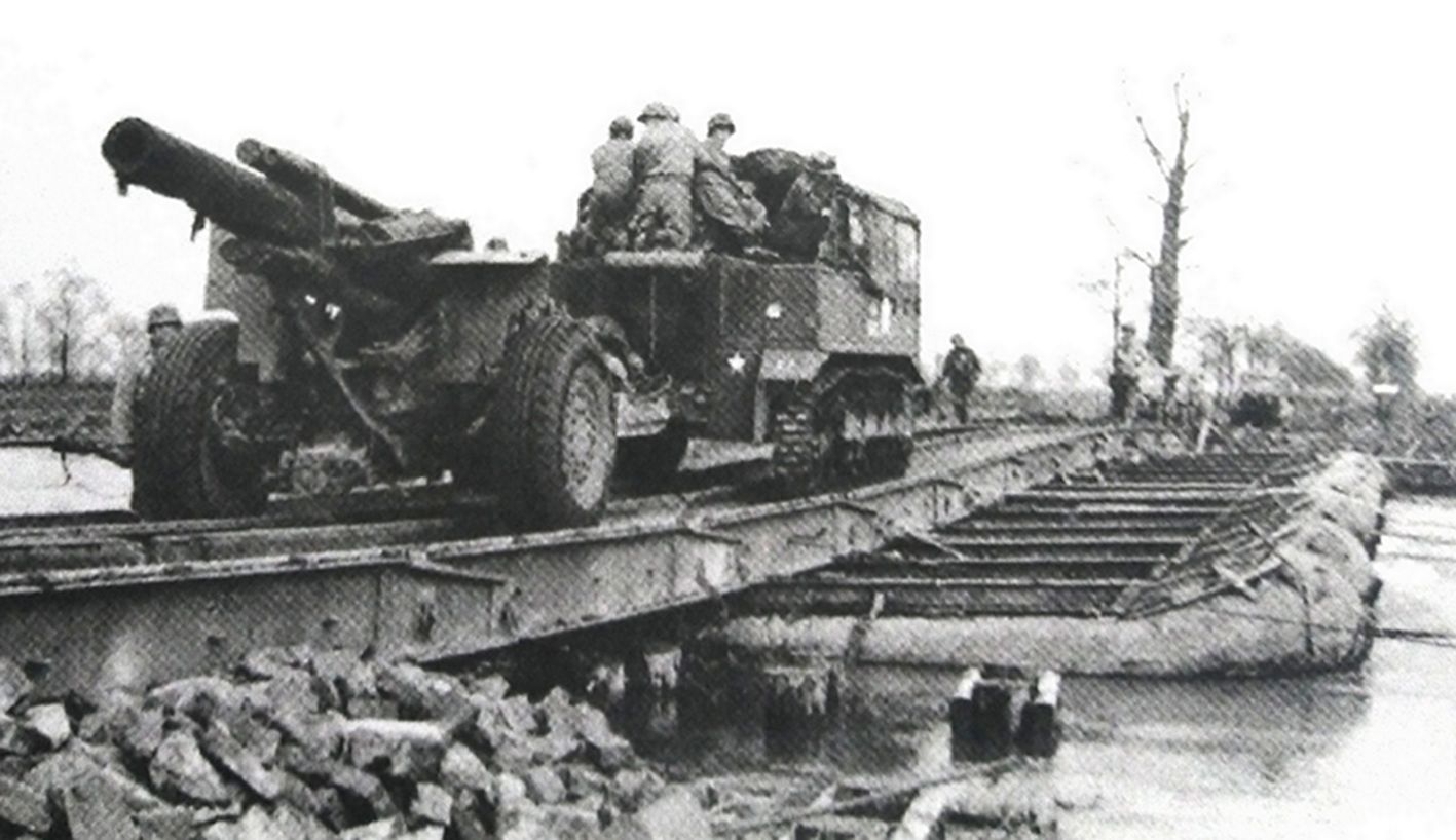 1945年3月，西线德国战场，来自美国第30步兵师第113野战炮兵营的一门M1（M114）式155毫米榴弹炮正途经鲁尔地区一条河流上的临时浮桥。
