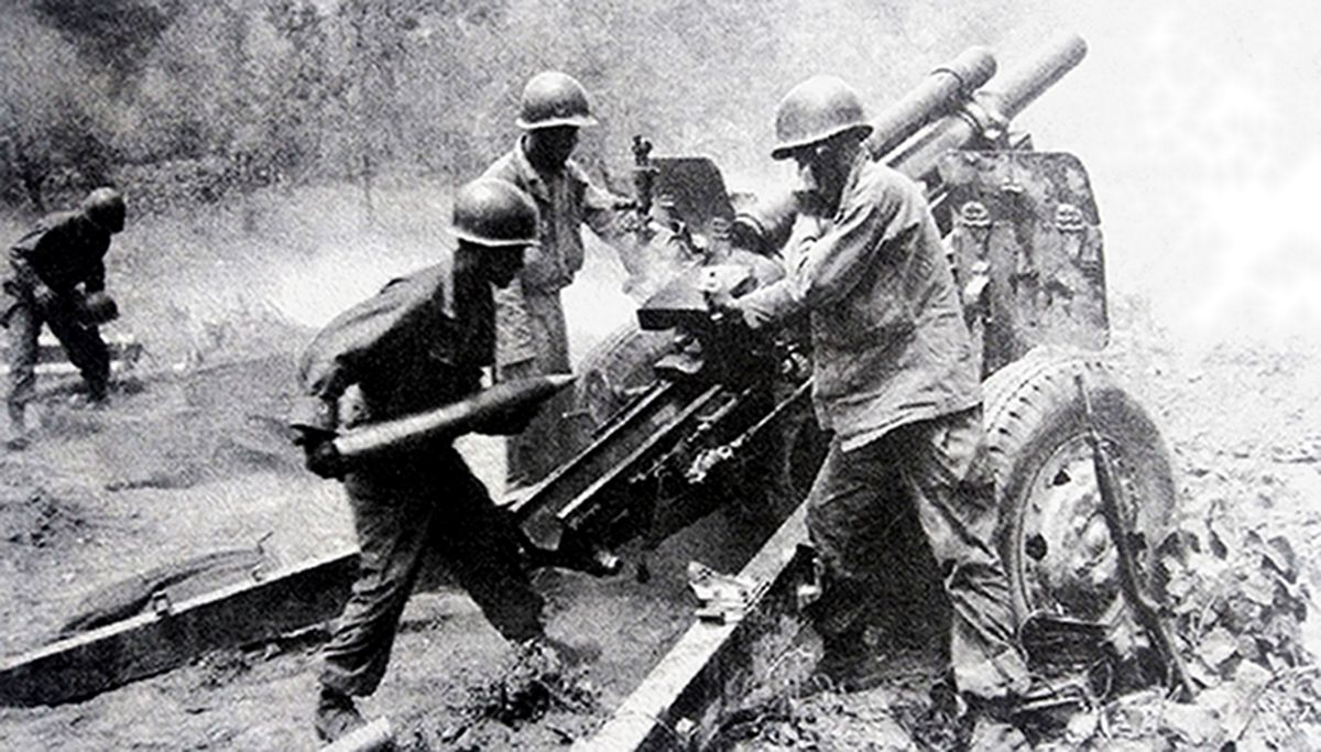 二战战场上，一门美军M2（M101）式105毫米榴弹炮正在战斗，美军炮兵正向炮膛装填炮弹。