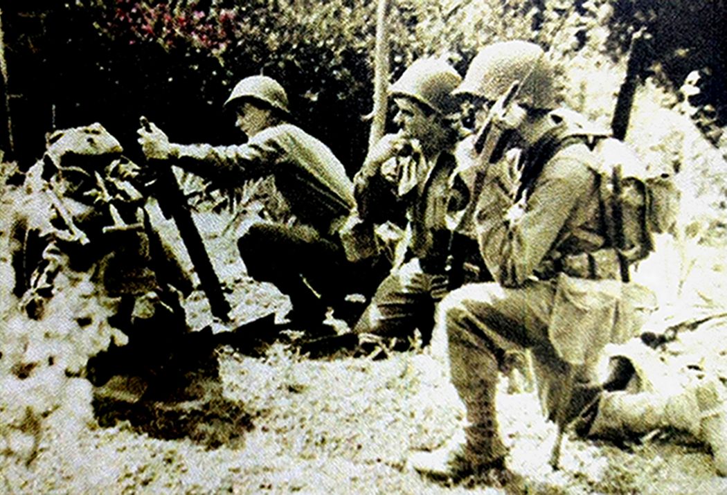 1944年8月，美军一门正在装弹发射的M2式60毫米迫击炮，右侧一名士兵正用SCR-586型手持对讲机与前线联络。