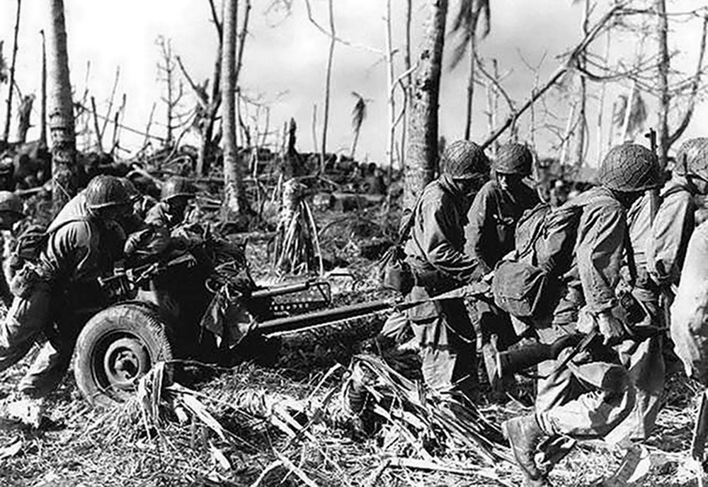 1944年，太平洋战场一处岛屿上，美军一个步兵炮班的炮兵们正合力拖着一门M3式37毫米反坦克炮转移阵地。图中树木已被炮火炸得七零八落，可知此处曾经历过激烈战斗。