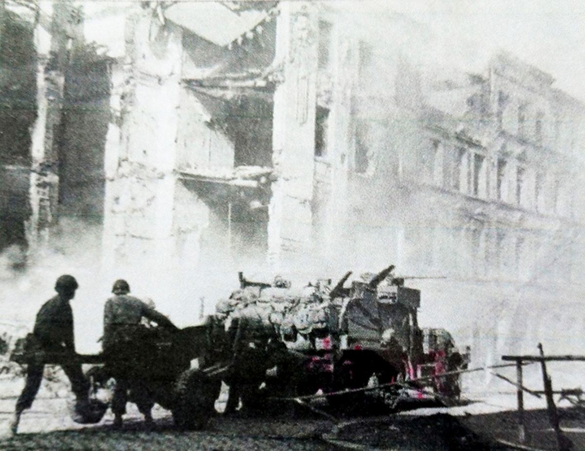 1944年10月15日，「亚琛战役」期间，德国亚琛的激烈战斗中，美军反坦克连的一辆M2A1半履带装甲车拖着一门M1A3式57毫米反坦克炮向前行进。作为西线战场上第一个遭到盟军攻击的德国城市，亚琛防御工事尤为坚固，美军攻入城后与德军展开巷战。作为英国6磅反坦克炮复制品的这型57毫米反坦克炮，在巷战攻坚中发挥了不少作用。