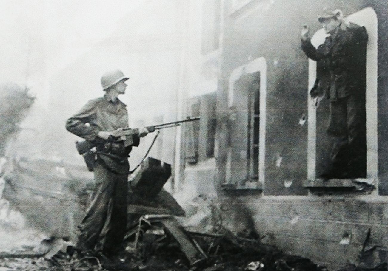 1945年，西线战场德国境内，美军一名士兵手持M1918A2「勃朗宁」自动步枪指向一名站在窗台的德军俘虏。