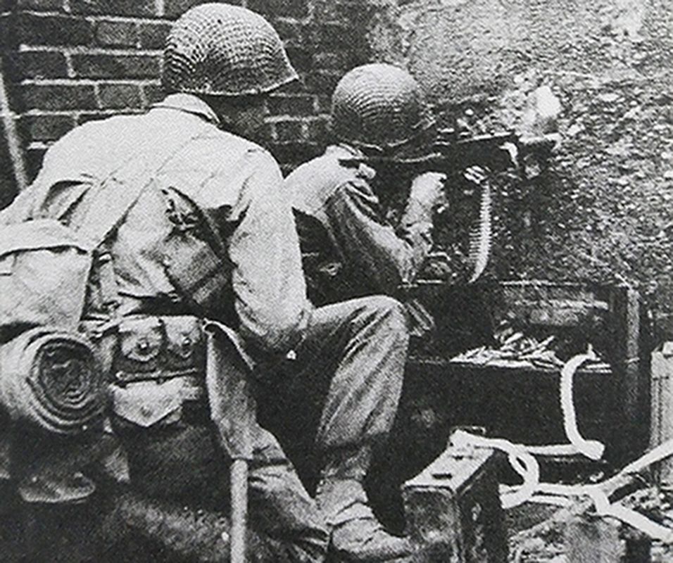 1944年10月，二战西线战场，一名隐蔽在房屋内的美军机枪手肩抵着一挺M1919A6重机枪，通过墙洞向外射击。
