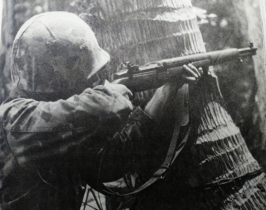 1945年春，太平洋战场，一名手持M1「加兰德」半自动步枪的美军士兵正以粗大树干为掩护，向日军目标瞄准射击。