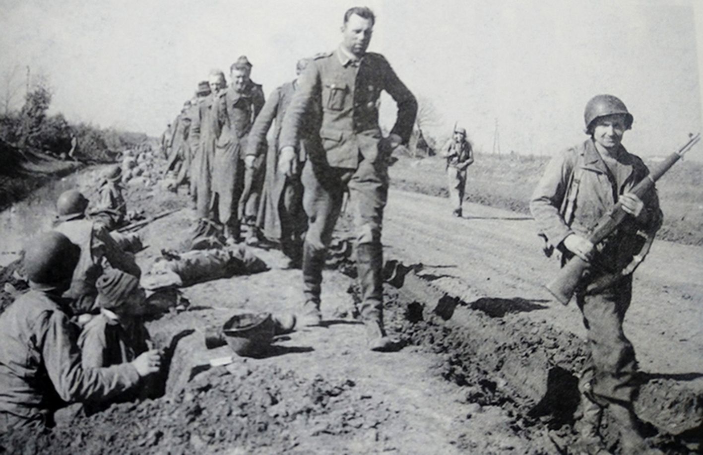 1944年初，「安齐奥战役」期间，西线战场意大利，盟军登陆安齐奥，在战斗中被俘的德军在美军士兵押解下向后方走去，最前方一位手持M1「加兰德」半自动步枪的押解士兵面向镜头，脸上带着胜利的微笑。