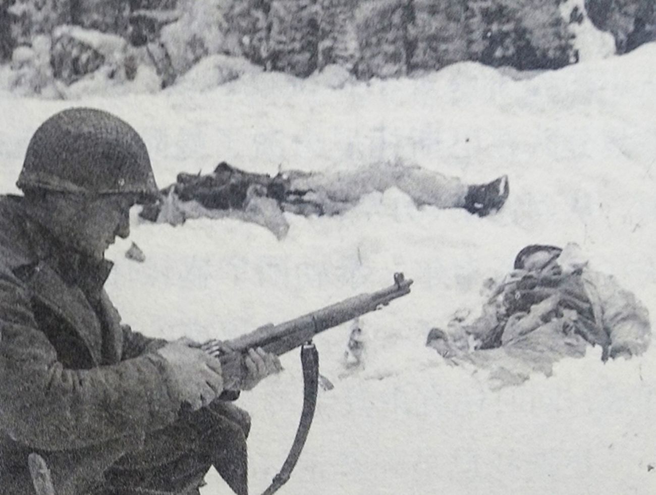 1944年冬季，西线战场比利时，美军第83师311步兵团3连一位名叫弗兰克·瓦卡辛的士兵正跪在雪地中，为手中的M1「加兰德」半自动步枪装弹，前方雪地上躺着两名被击毙的德军士兵。