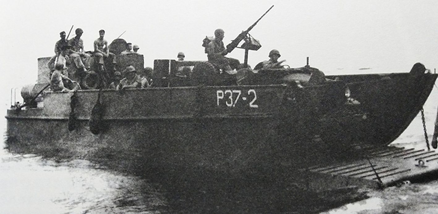 1944年5月,「塞班岛战役」期间,太平洋战场塞班岛,美军一艘两栖登陆艇正在红滩登陆,艇上载有一辆安装了M2重机枪的一吨卡车和一批士兵。