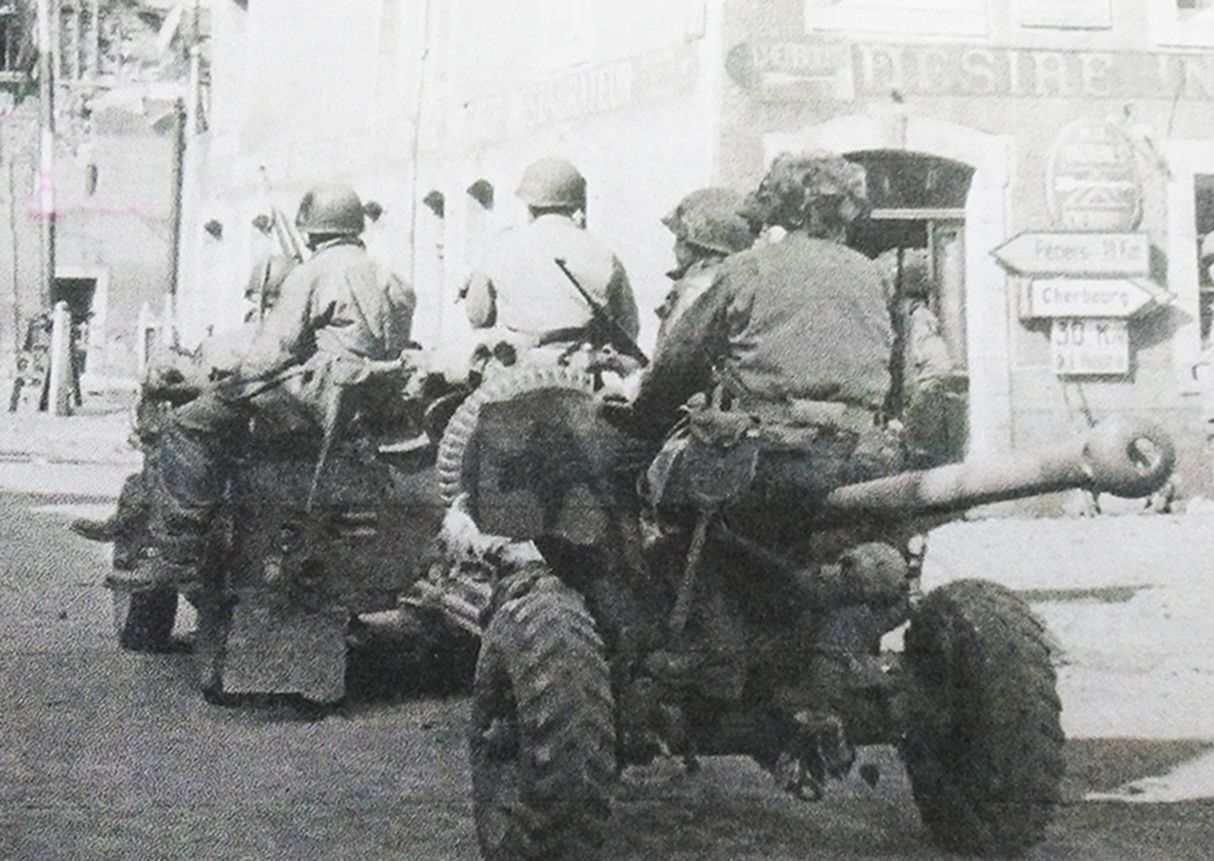 1944年夏天，「诺曼底登陆」期间，西线法国战场，在诺曼底地区降落的美军空降师士兵用吉普车牵引着一门空降的英式6磅反坦克炮穿过一座村庄，坐在火炮上的一名美军拿着M3冲锋枪。