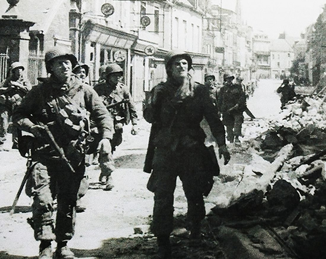 1944年夏天，「诺曼底登陆」期间，西线法国战场，美军空降兵正穿过瑟堡半岛的卡伦坦，该城镇刚经历一场激烈战斗，一名拿着M3冲锋枪的士兵带着胜利微笑走在最前面。